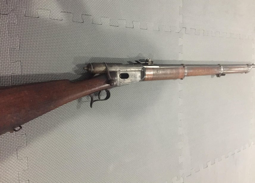 A vintage bolt-action rifle with a wooden stock and metal barrel rests on a gray textured foam mat, positioned diagonally from the bottom left to the top right of the image.