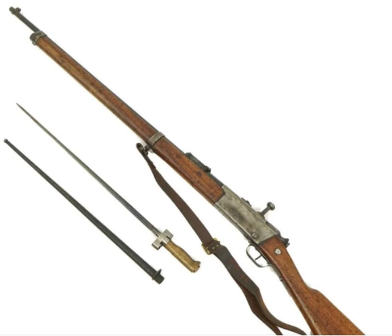 A vintage bolt-action rifle with a wooden stock is shown alongside a long bayonet and its metal scabbard, set on a white background. The rifle has a leather sling attached.