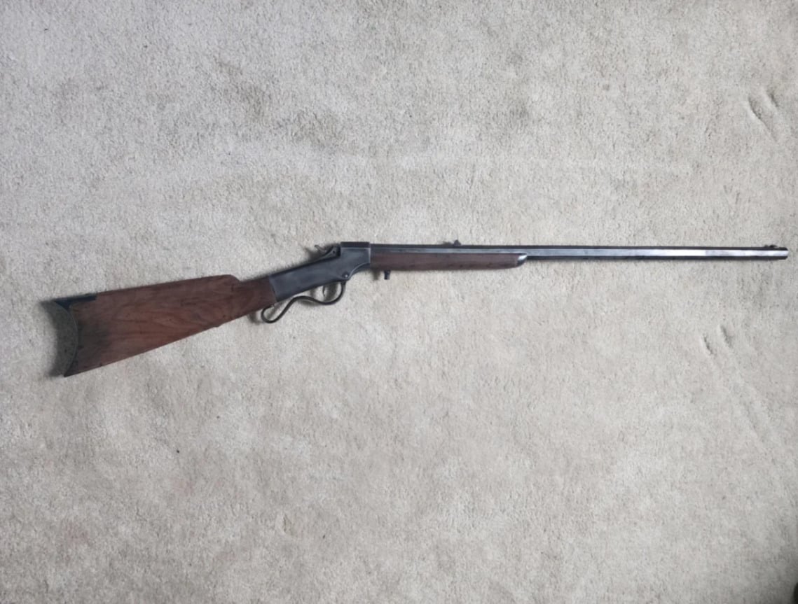 A vintage lever-action rifle with a wooden stock and metal barrel, lying on a light-colored carpeted floor.