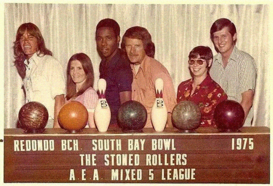 Six people stand behind a row of bowling balls and pins, smiling. A sign in front reads: "Redondo BCH. South Bay Bowl 1975 The Stoned Rollers A.E.A. Mixed 5 League.