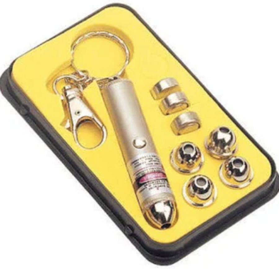 A set containing a silver laser pointer keychain, metal keyring, three small batteries, four silver caps, and extra battery holders, all arranged in a black and yellow foam case.