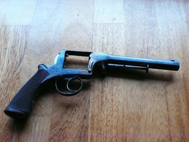 An antique pepperbox-style pistol with an ornate metal frame and textured grip lies on a wooden surface.