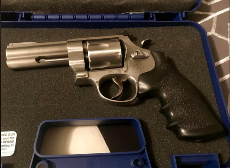 A silver revolver with a black grip is displayed in a foam-lined blue case, with an empty compartment beneath it and part of a striped fabric visible in the background.