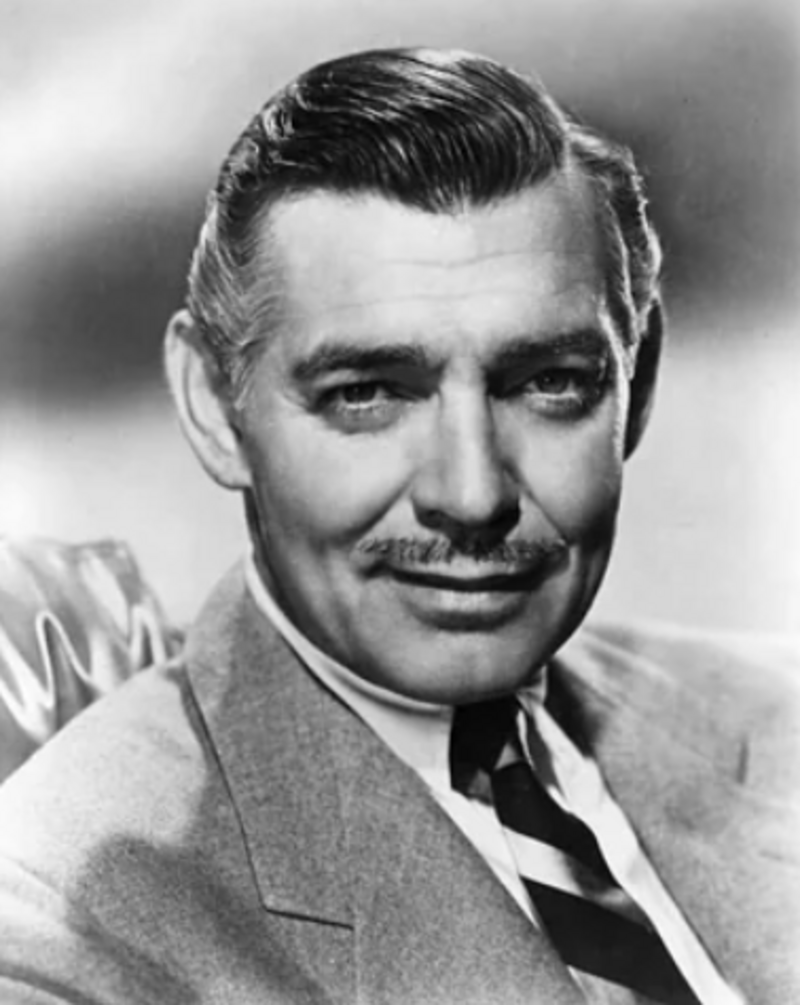 A black-and-white portrait of a man in a suit and tie, with neatly combed hair and a mustache, smiling slightly while looking at the camera.