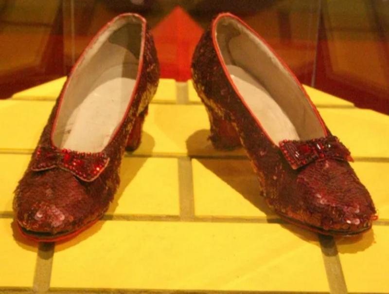 A pair of sequined red shoes with bows are displayed on a yellow-tiled surface, inspired by the iconic ruby slippers from "The Wizard of Oz.