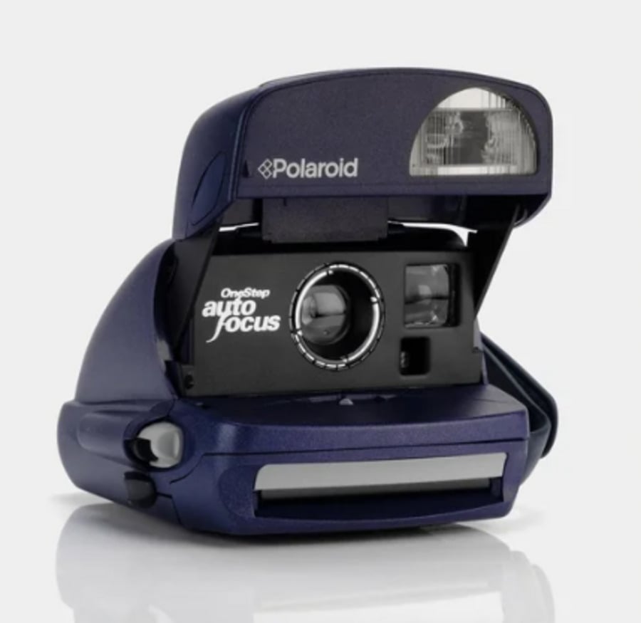 A dark blue Polaroid OneStep camera with auto focus, open and ready to take a photo, showing its lens, flash, and branding on a plain light background.