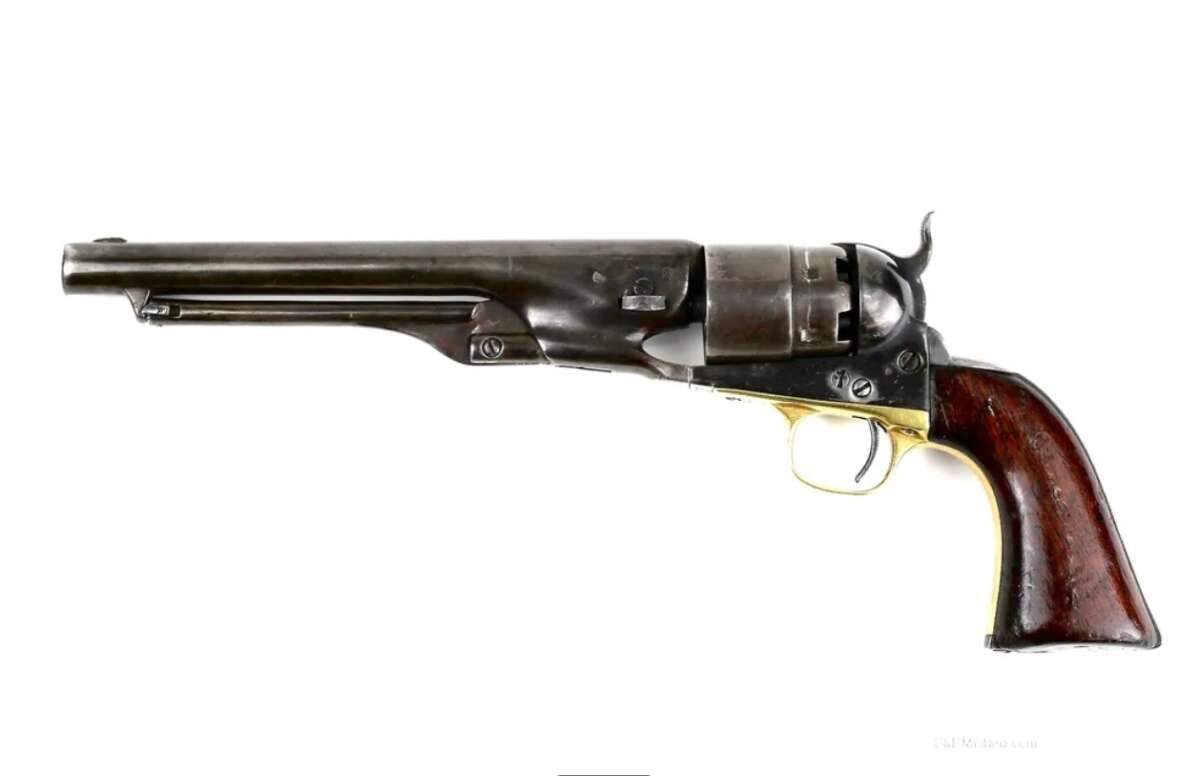 A vintage black powder revolver with a long barrel, dark metal finish, brass trigger guard, and a wooden grip, shown in a side profile view on a white background.