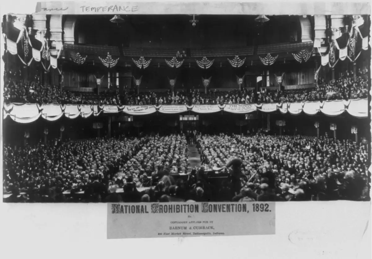 A large crowd fills a decorated auditorium for the National Prohibition Convention in 1892. American flags and bunting hang from balconies above the audience, and a sign with the event’s name is displayed at the front.