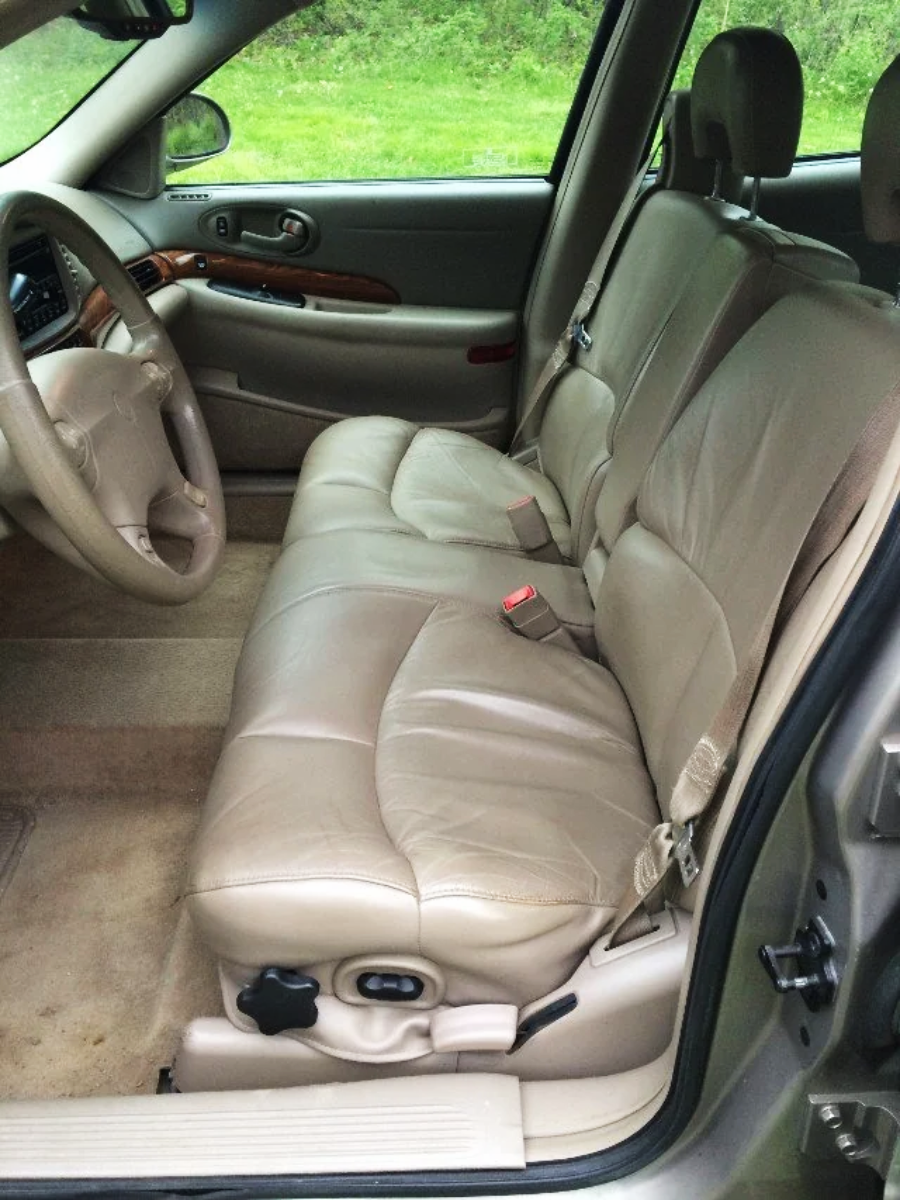 The interior of a car with beige leather seats, a tan carpeted floor, and a wooden trim on the door and dashboard. The photo is taken from the passenger side, showing the front and back seats.