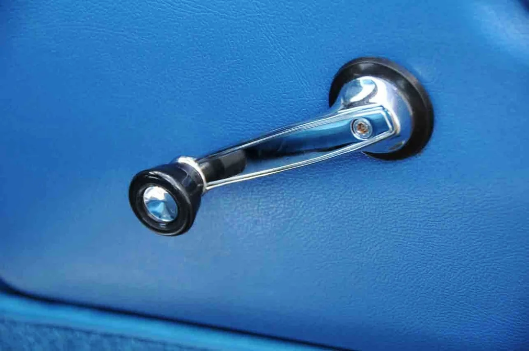 A close-up of a car's manual window crank handle with a chrome finish, mounted on a blue door panel.