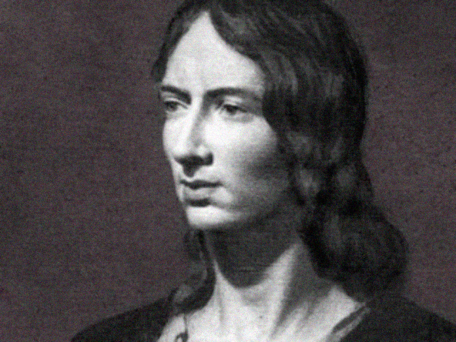 A black and white portrait of a woman with long, wavy hair, wearing a dark garment, looking slightly to the side with a calm, composed expression. The background is plain and muted.