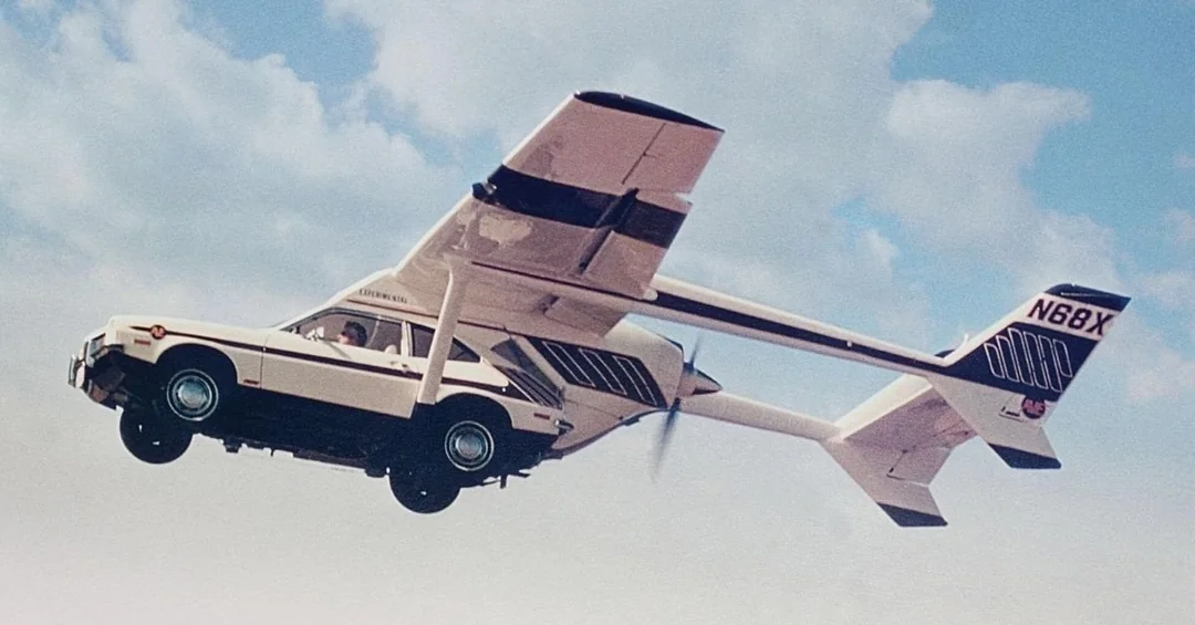 A flying car with wings and a propeller is airborne against a cloudy sky. The vehicle has a car body with attached aircraft wings and tail. The registration number N68X is visible on the tail.
