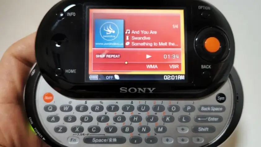 A hand holds a Sony handheld device with a slide-out keyboard. The screen displays a music player interface, showing a song titled "And You Are" by Swandive, with playback controls below.