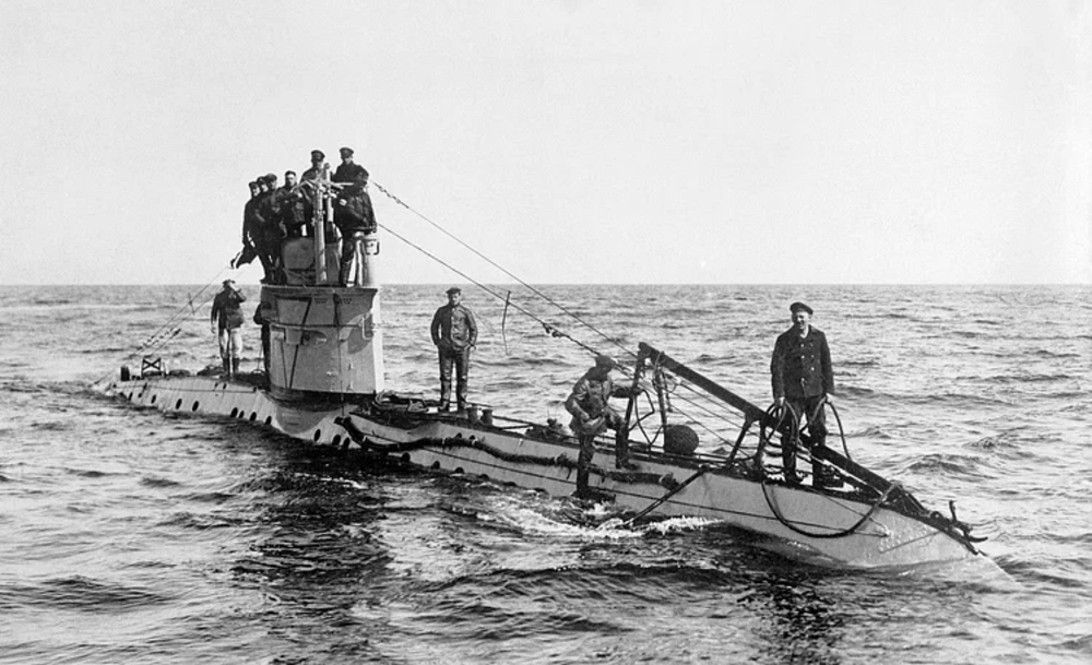 Black-and-white photo of a World War I-era submarine at sea with several crew members standing on its deck and tower. The sea is calm and the horizon is visible in the background.