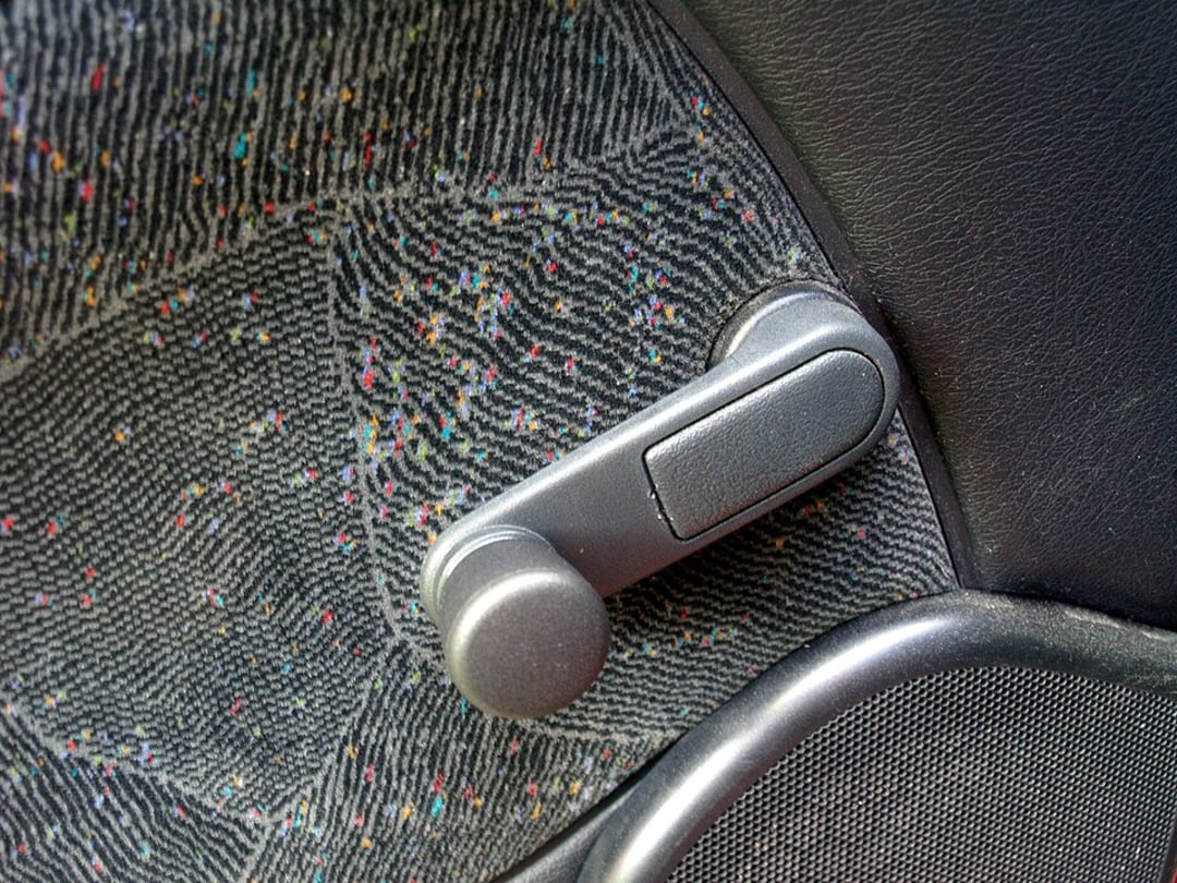 Close-up of a manual car window crank handle on a patterned fabric car door panel.