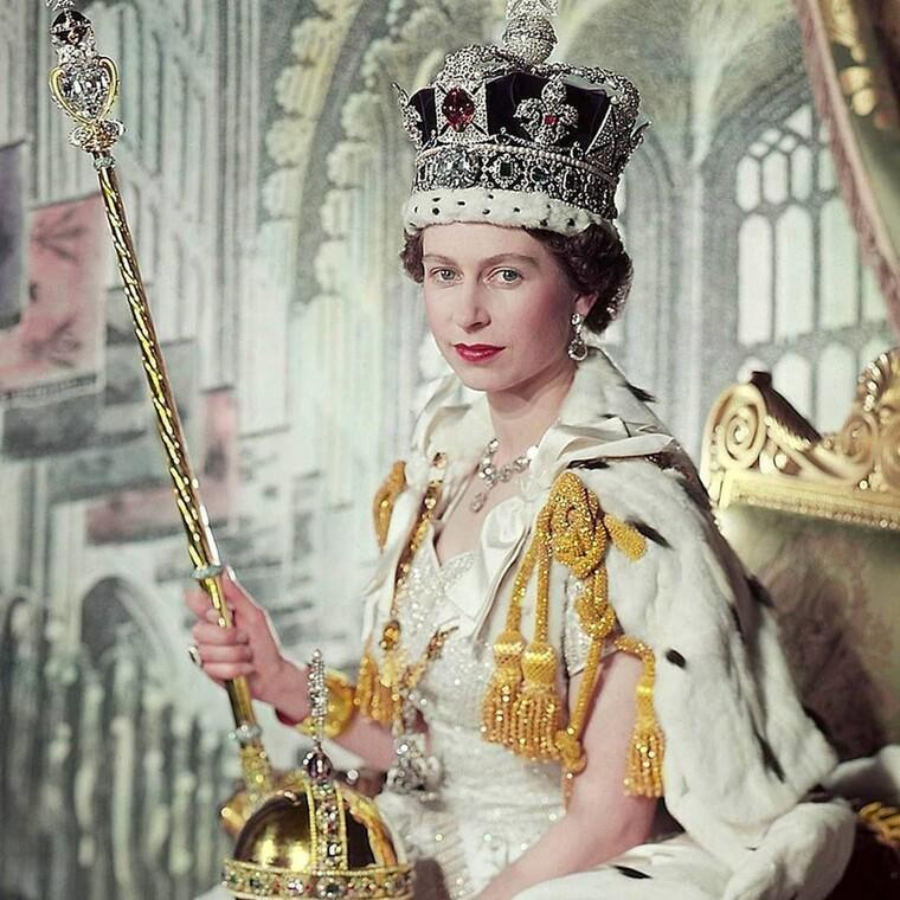A woman in royal attire sits on a golden throne, wearing a jeweled crown and holding a scepter. She is dressed in a white robe with fur trim and ornate decorations, with a golden orb placed in front of her.