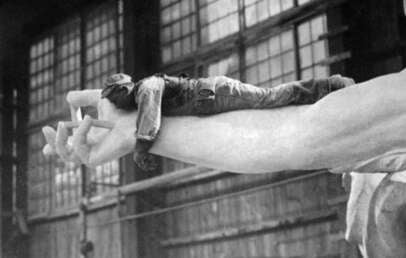 A worker lies on the large outstretched hand of the unfinished Statue of Liberty inside a construction workshop with large windows in the background.