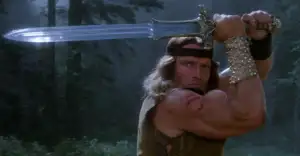 A muscular man with long hair and a headband holds a large sword above his head, ready to strike, standing in a forest with a determined expression. He wears a studded arm cuff and has scars on his shoulder.