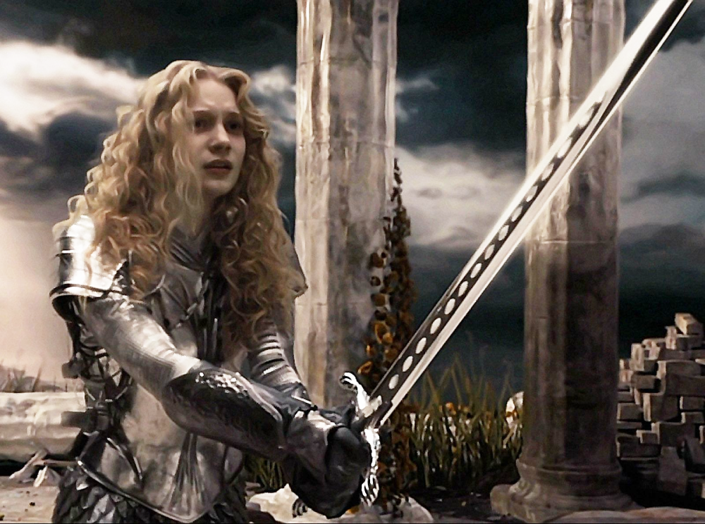 A young woman in silver armor with long curly blonde hair holds a large sword with both hands, standing among ancient stone ruins under a dramatic, cloudy sky.