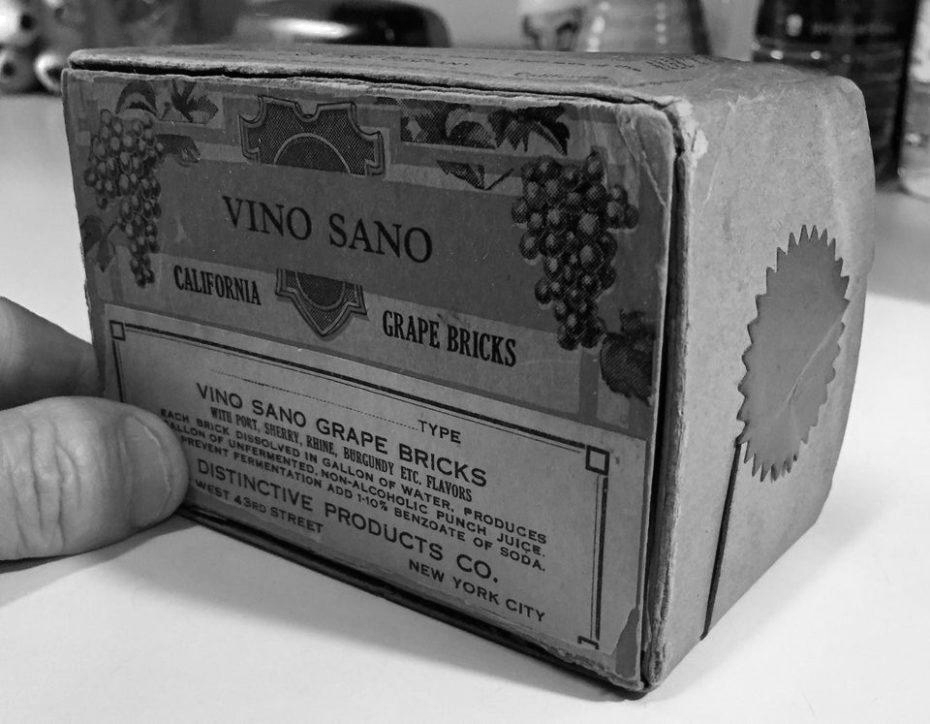 A hand holds a vintage box labeled "Vino Sano California Grape Bricks" with grapevine illustrations and product information printed on the packaging in black and white.