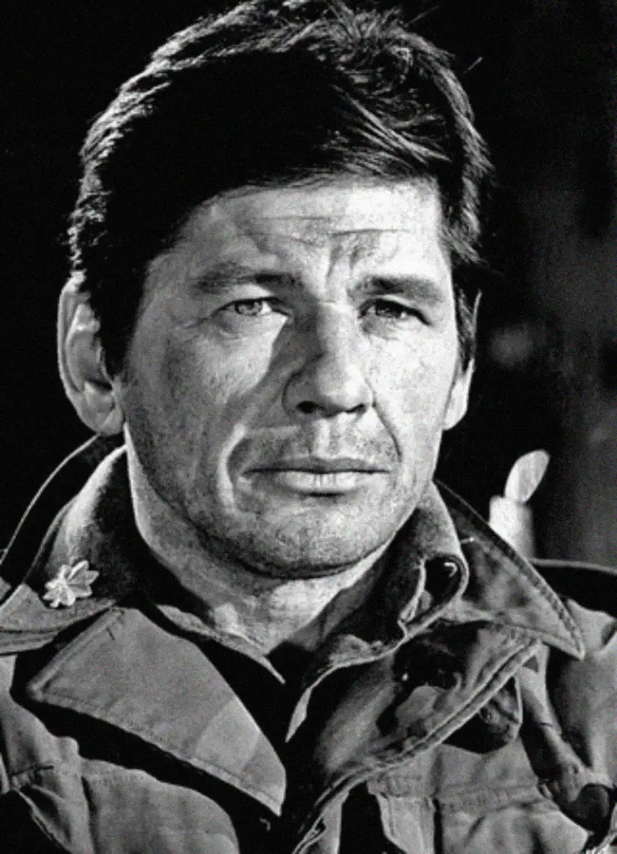 Black and white portrait of a man with dark hair, wearing a military-style jacket, looking slightly to the side with a serious expression.