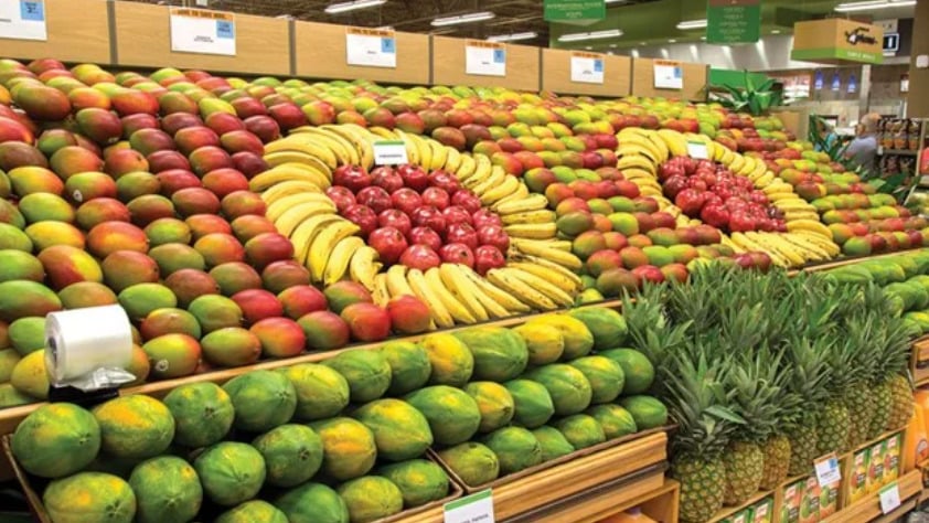 Colorful fruit display in a grocery store, featuring mangoes, papayas, pineapples, bananas arranged in circles, and apples in the center, creating an eye-catching pattern on wooden shelves.