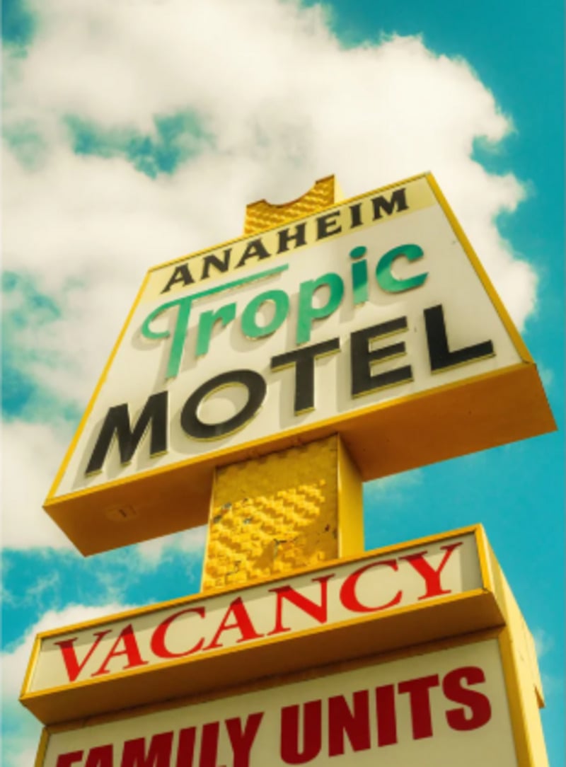 A retro motel sign against a blue sky with clouds reads "Anaheim Tropic Motel" with "Vacancy" and "Family Units" displayed below in bold red and yellow letters.