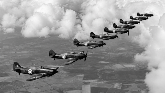 Eight vintage military aircraft fly in formation above the clouds over patchwork fields. The planes display roundels on their wings and tails, suggesting they are from the Royal Air Force. The image is in black and white.