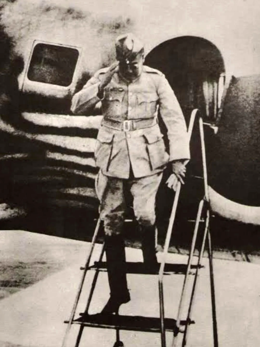 A person in military uniform salutes while descending steps from an aircraft in a black-and-white historical photograph.