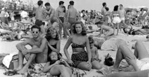 Black and white photo of people enjoying a day at the beach in the 1950s