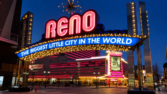Neon-lit Reno arch at night reads “RENO: THE BIGGEST LITTLE CITY IN THE WORLD,” with casinos and lights in the background under a dark blue sky.