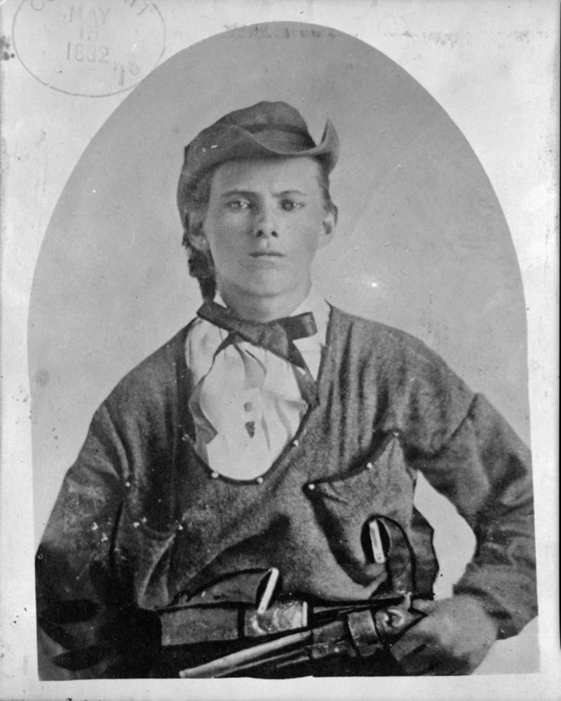 Black-and-white portrait of a young person wearing a cap, loose shirt, and scarf, holding a revolver at their waist. The image has an oval frame and a visible stamp in the top left corner dated 1882.