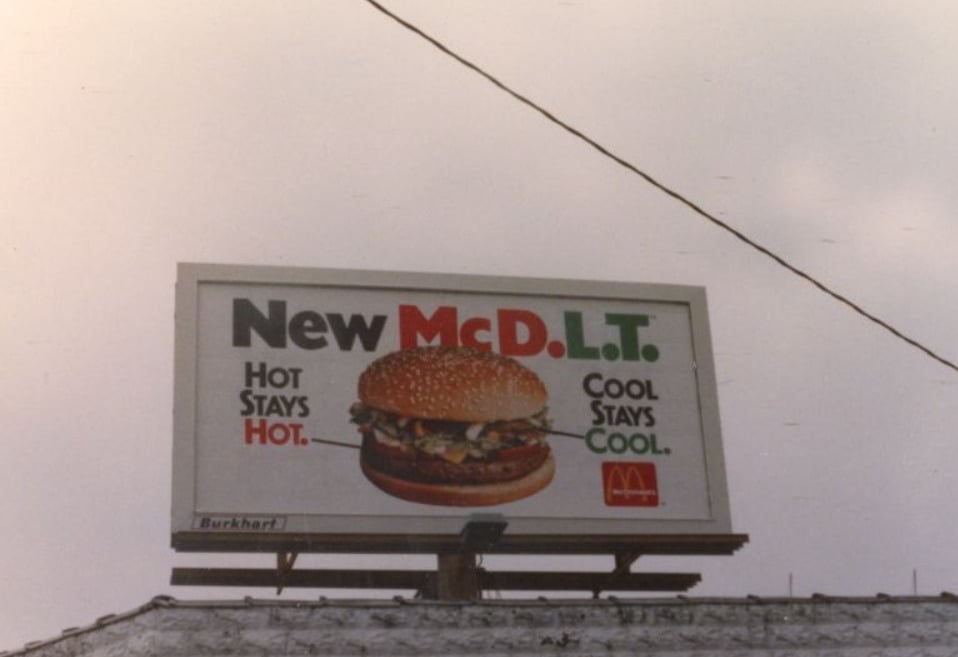 A billboard advertises the McDonald's McDLT burger, showing a burger image and the slogan: “New McDLT. Hot stays hot. Cool stays cool.” The McDonald’s logo is visible on the bottom right.
