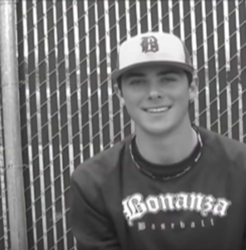 Young man in a baseball cap and "Bonanza Baseball" sweatshirt smiles while sitting in front of a chain-link fence. The image is in black and white.