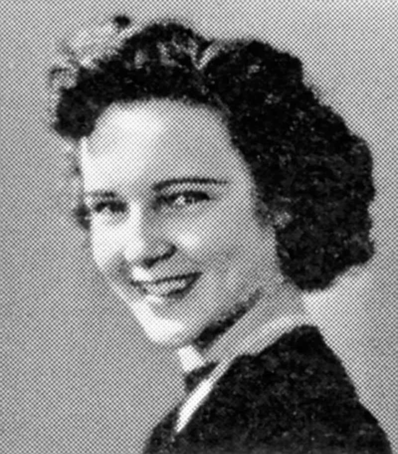 A black and white portrait of a young woman with curly hair, smiling and looking slightly to the side. She is wearing a dark top with a light collar. The background is plain.
