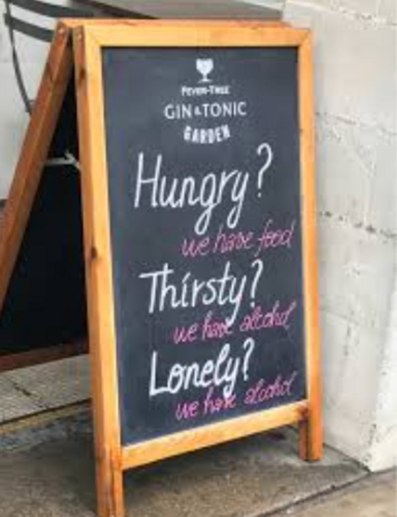 A chalkboard sign outside a bar reads: "Hungry? we have food. Thirsty? we have alcohol. Lonely? we have alcohol." The sign promotes drinks and food in a playful tone.