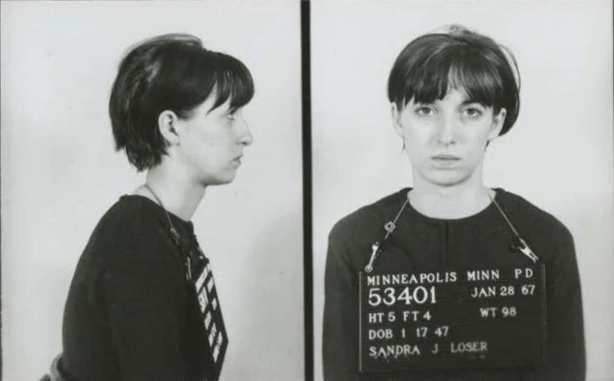A black-and-white mugshot photo showing a woman with short dark hair. The left image is a side profile; the right is a front view. She holds a sign with personal details and "Minneapolis Minn PD" written on it.