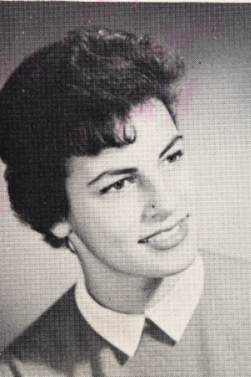 Black and white portrait of a young woman with short, wavy hair, wearing a light-colored collared top and looking slightly to the side with a gentle smile.