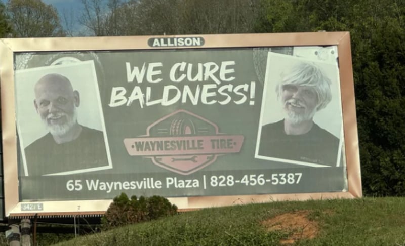 A roadside billboard shows two photos of an older, bearded man—one bald and one with thick, white hair. The sign reads, "We cure baldness! Waynesville Tire," with an address and phone number at the bottom.