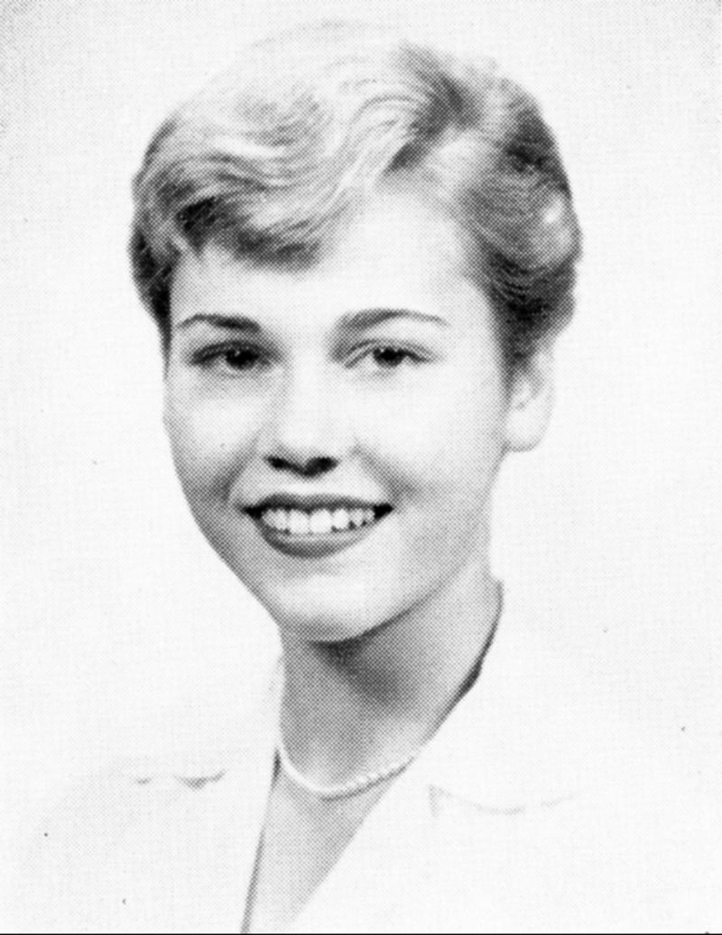 Black and white portrait of a young woman with short, light hair, smiling, wearing a light-colored top and a necklace, posed against a plain background.