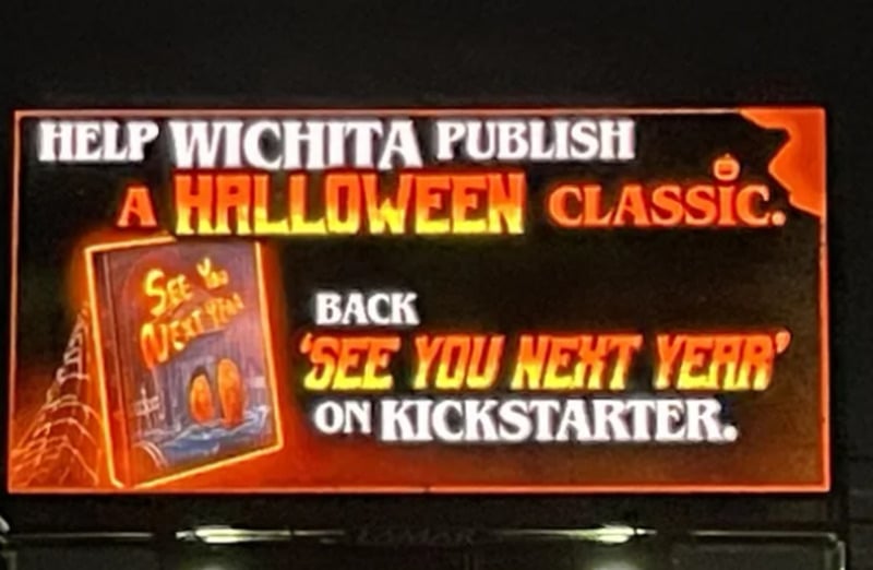 A billboard reads: "Help Wichita publish a Halloween classic. Back 'See You Next Year' on Kickstarter." It features a spooky book cover with a spiderweb, pumpkins, and glowing orange text.
