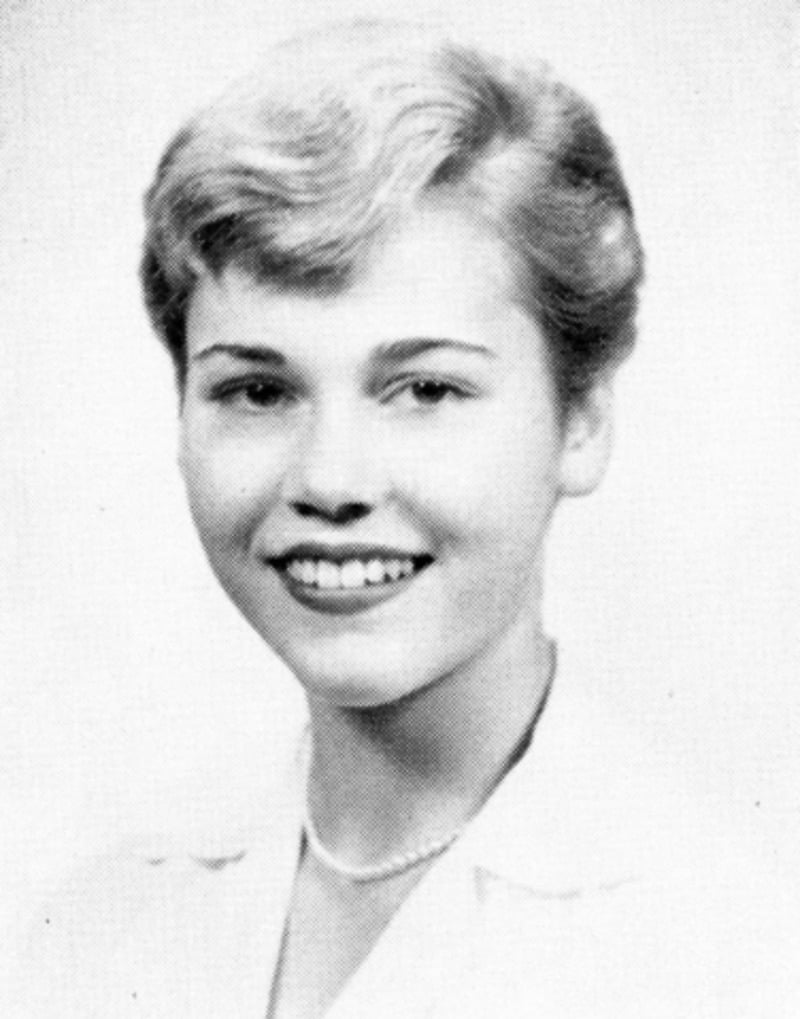 Black and white portrait of a young woman with short, light-colored hair, smiling and wearing a light-colored top and a simple necklace.