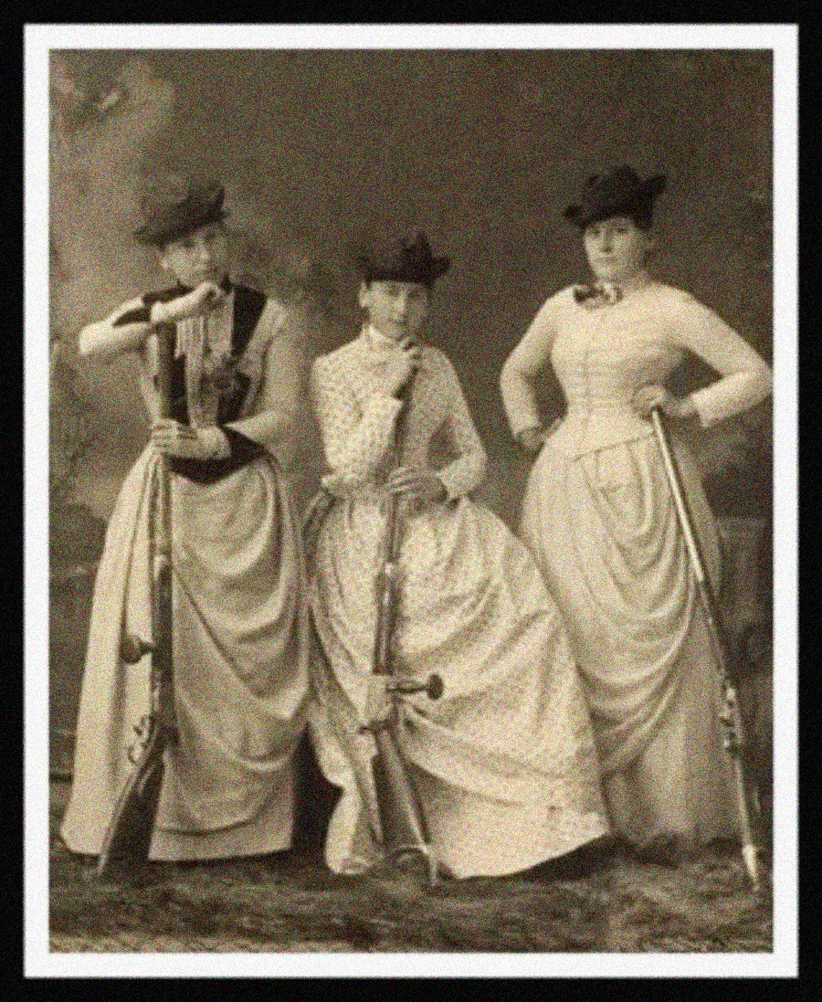 Three women in Victorian-era dresses and hats pose for a vintage photograph, each holding a large rifle. The setting has a painted backdrop and the women stand confidently, gazing at the camera.