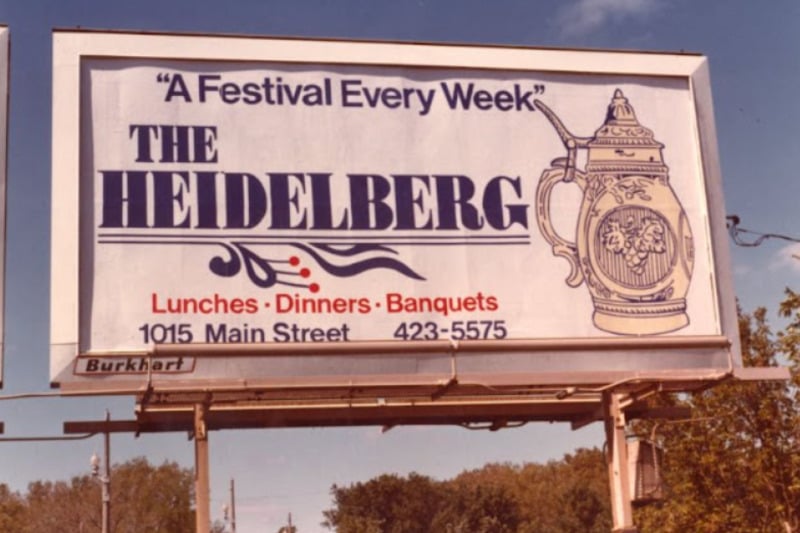 A billboard advertising "The Heidelberg" with the slogan "A Festival Every Week," and offering lunches, dinners, and banquets. Address and phone number are also listed. An image of a beer stein decorates the sign.