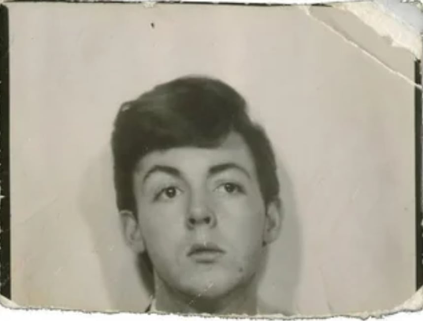 A young man with dark hair looks slightly upward in a worn, black-and-white portrait photo. The edges of the photograph are creased and damaged, giving it a vintage appearance.