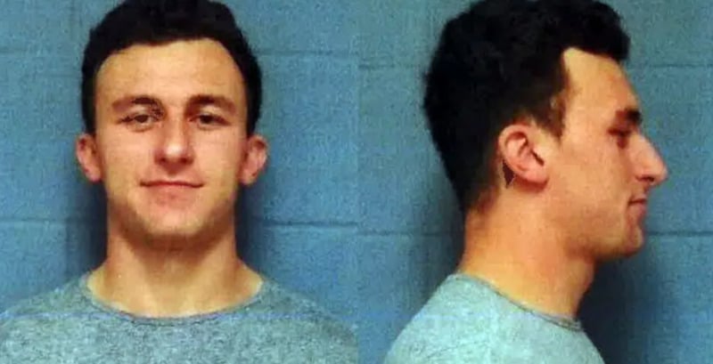 A young man with short dark hair wearing a light gray shirt is shown in a police mugshot, facing forward and to the right, against a plain blue background.