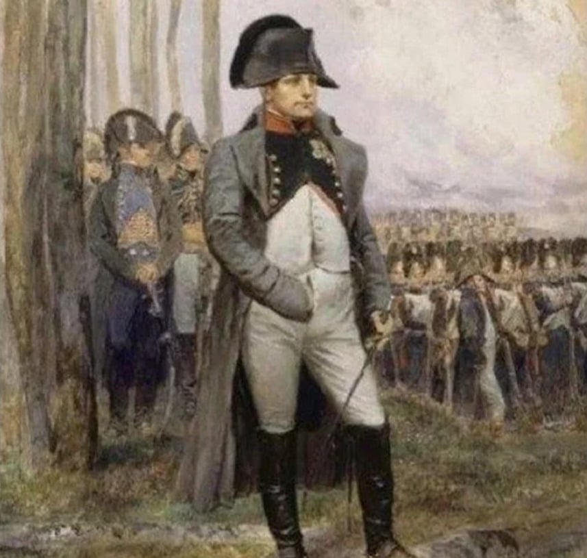 A man in historical military uniform and a black hat stands with one hand inside his coat, surrounded by officers and soldiers in formation in a wooded outdoor setting.