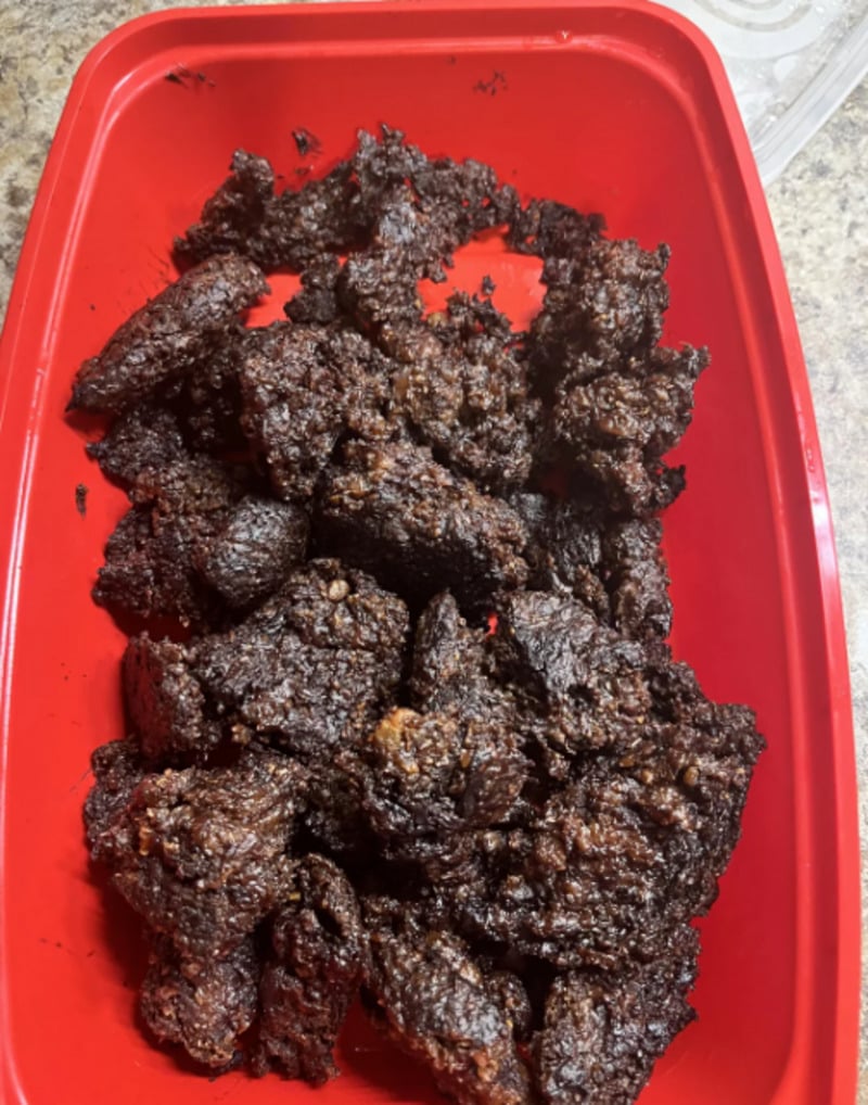 Chunks of dark, dense, unevenly textured baked dessert are arranged in a red rectangular container on a kitchen countertop. The pieces look crumbly and moist.