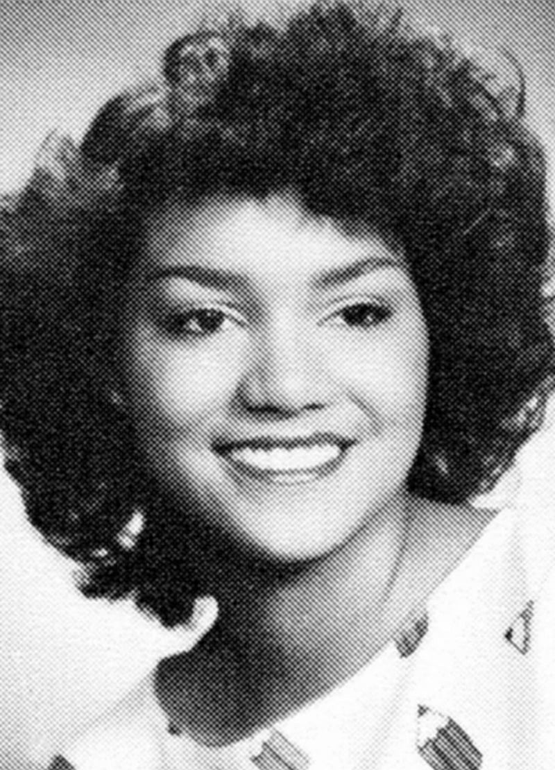 Black and white portrait of a young woman with curly hair, smiling and looking slightly to the side, wearing a light-colored top with a subtle pattern.
