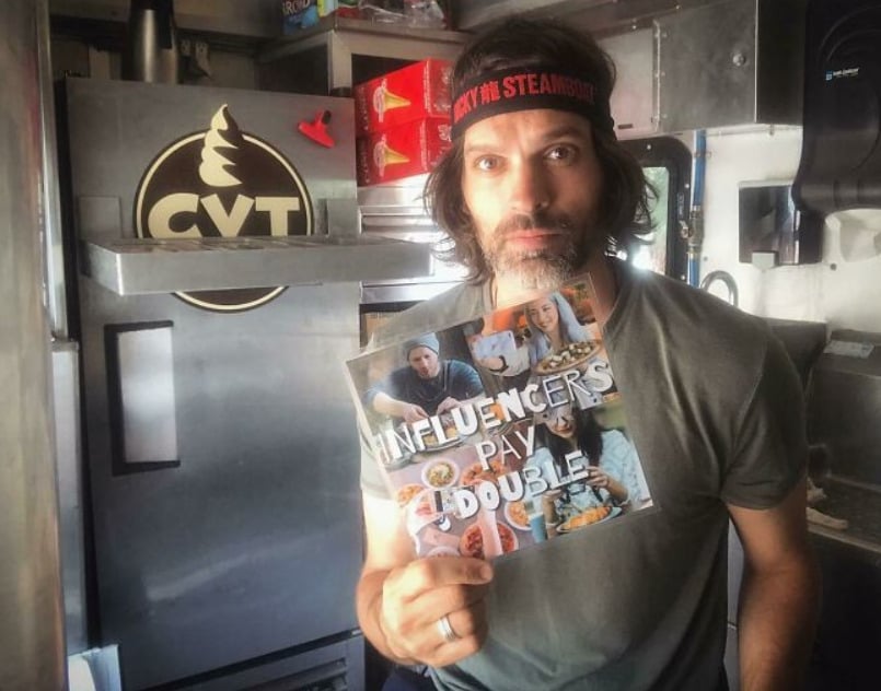 A man in a headband stands in a food truck holding a sign with food photos that reads "INFLUENCERS PAY DOUBLE." The background shows an ice cream machine and shelves with supplies.
